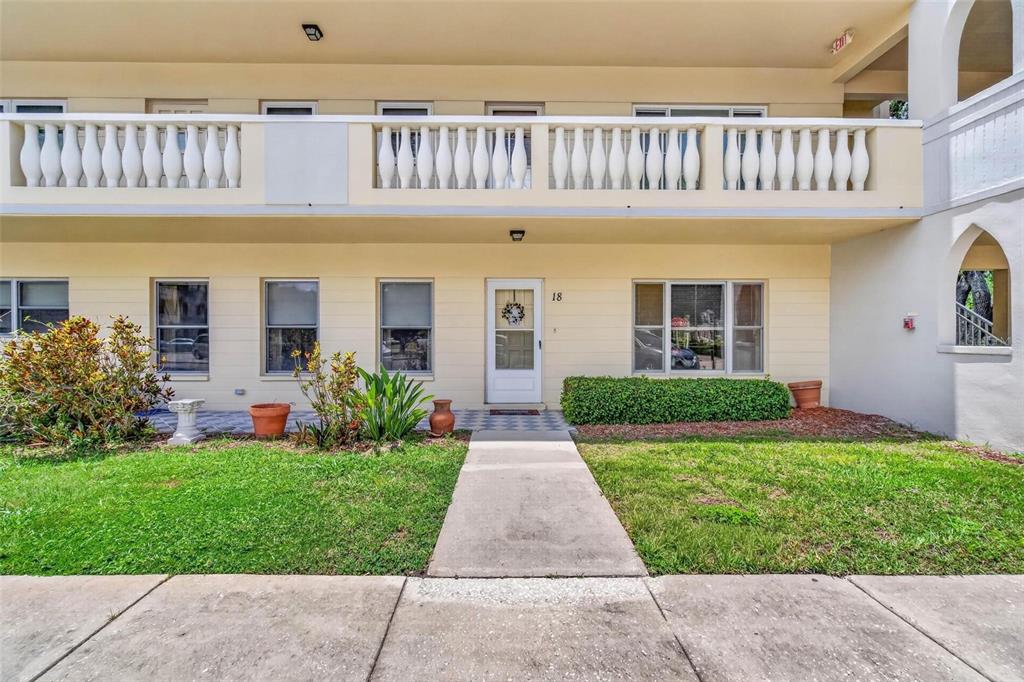 A two-story building exterior features a white front door, a balcony, and a concrete walkway — 2222 AMERICUS BOULEVARD N UNIT 18, CLEARWATER, FL
