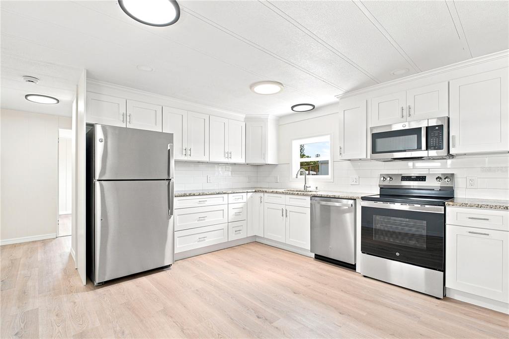 A kitchen with white cabinets, stainless steel appliances, and light wood-look flooring — 6711 CLEMENS BOULEVARD, PORT RICHEY, FL