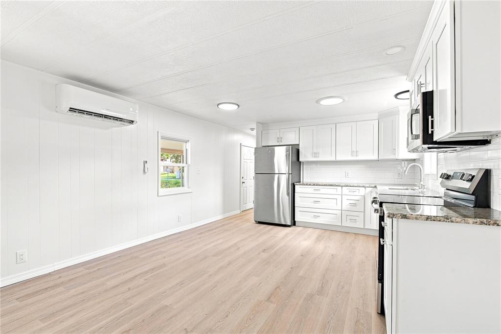 A bright kitchen features white cabinets, stainless steel appliances, and light wood-look flooring — 6711 CLEMENS BOULEVARD, PORT RICHEY, FL