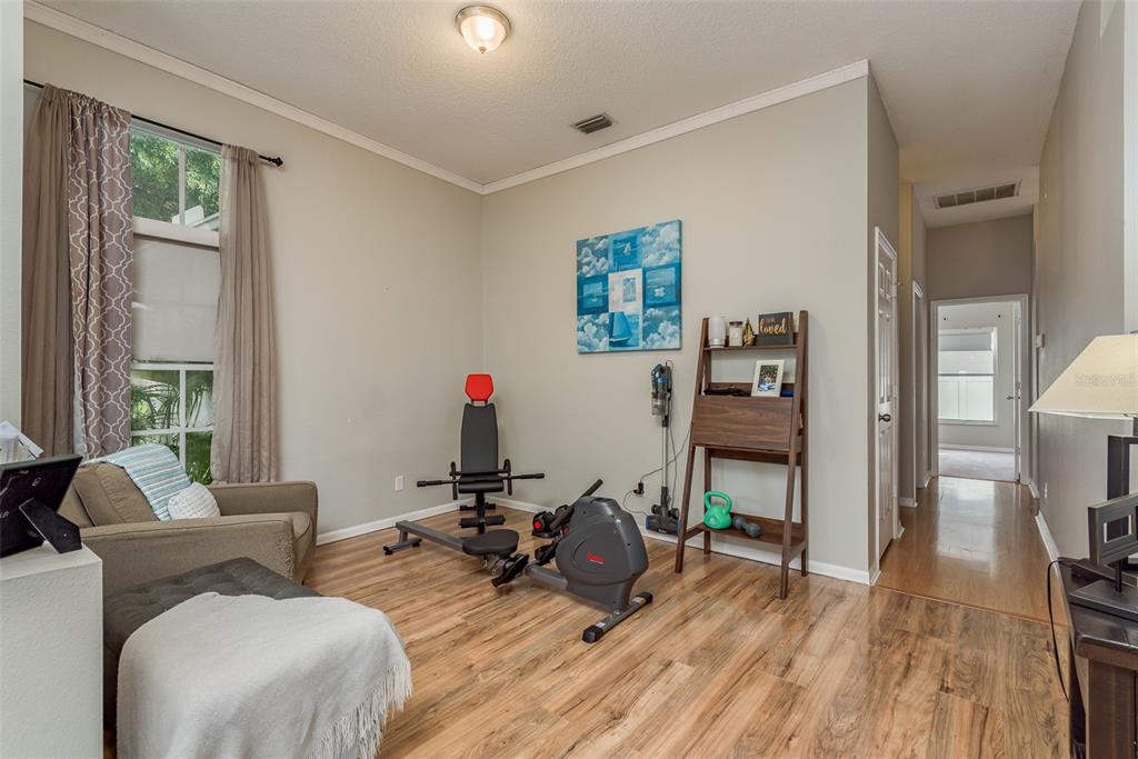 A multi-purpose room features wood-look flooring, exercise equipment, a chair, and a decorative ladder shelf — 28739 COTTAGEWOOD DRIVE, WESLEY CHAPEL, FL