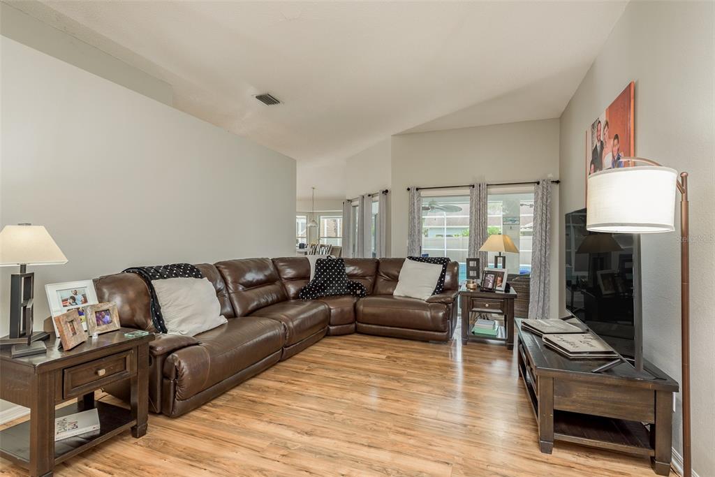 A living room features a brown leather sectional, wood-look flooring, and a television on a stand — 28739 COTTAGEWOOD DRIVE, WESLEY CHAPEL, FL