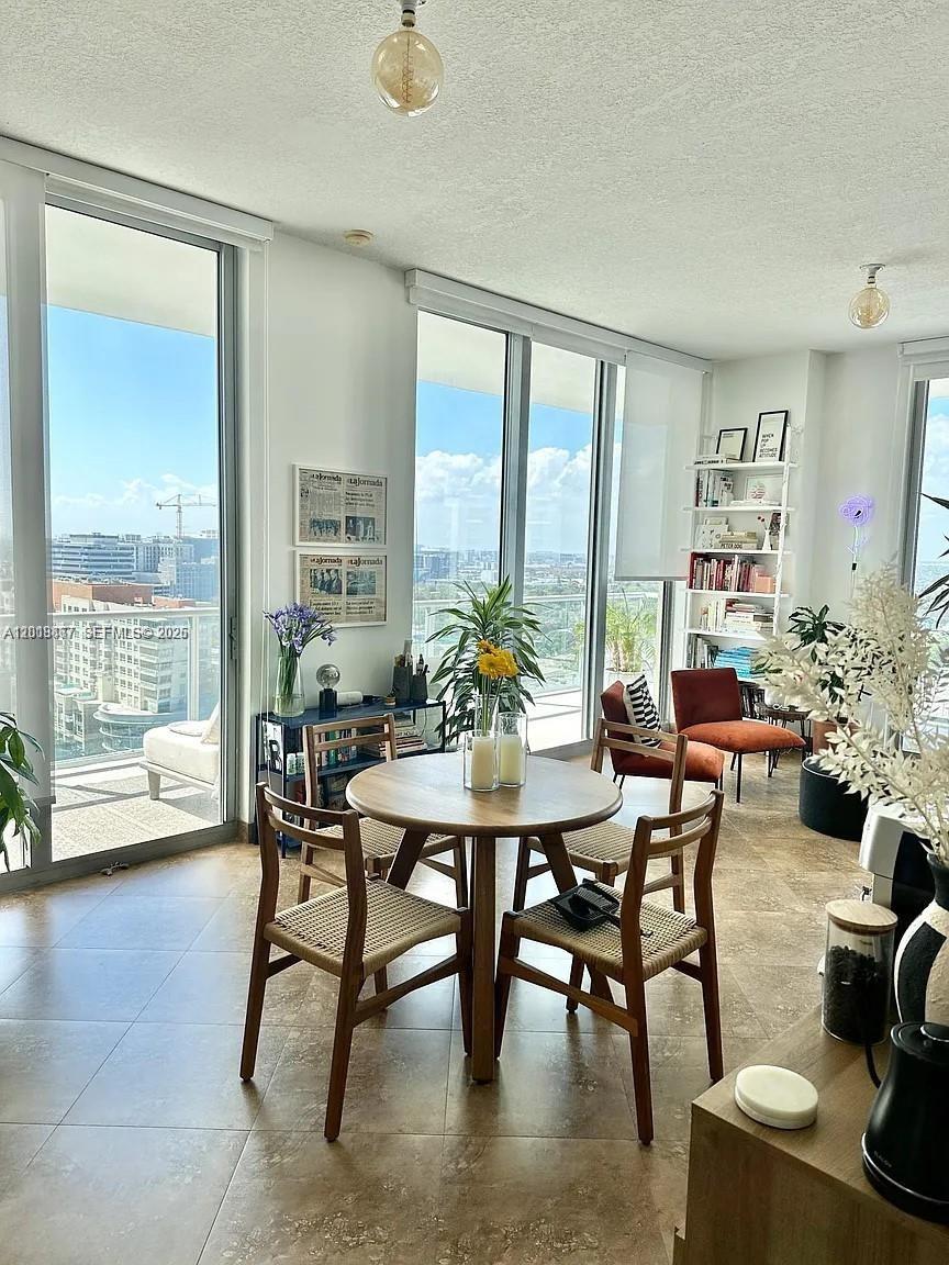 A dining area with a round wooden table and chairs sits before floor-to-ceiling windows — 3470 E Coast Ave # H1805, Miami FL 33137, MIAMI, FL