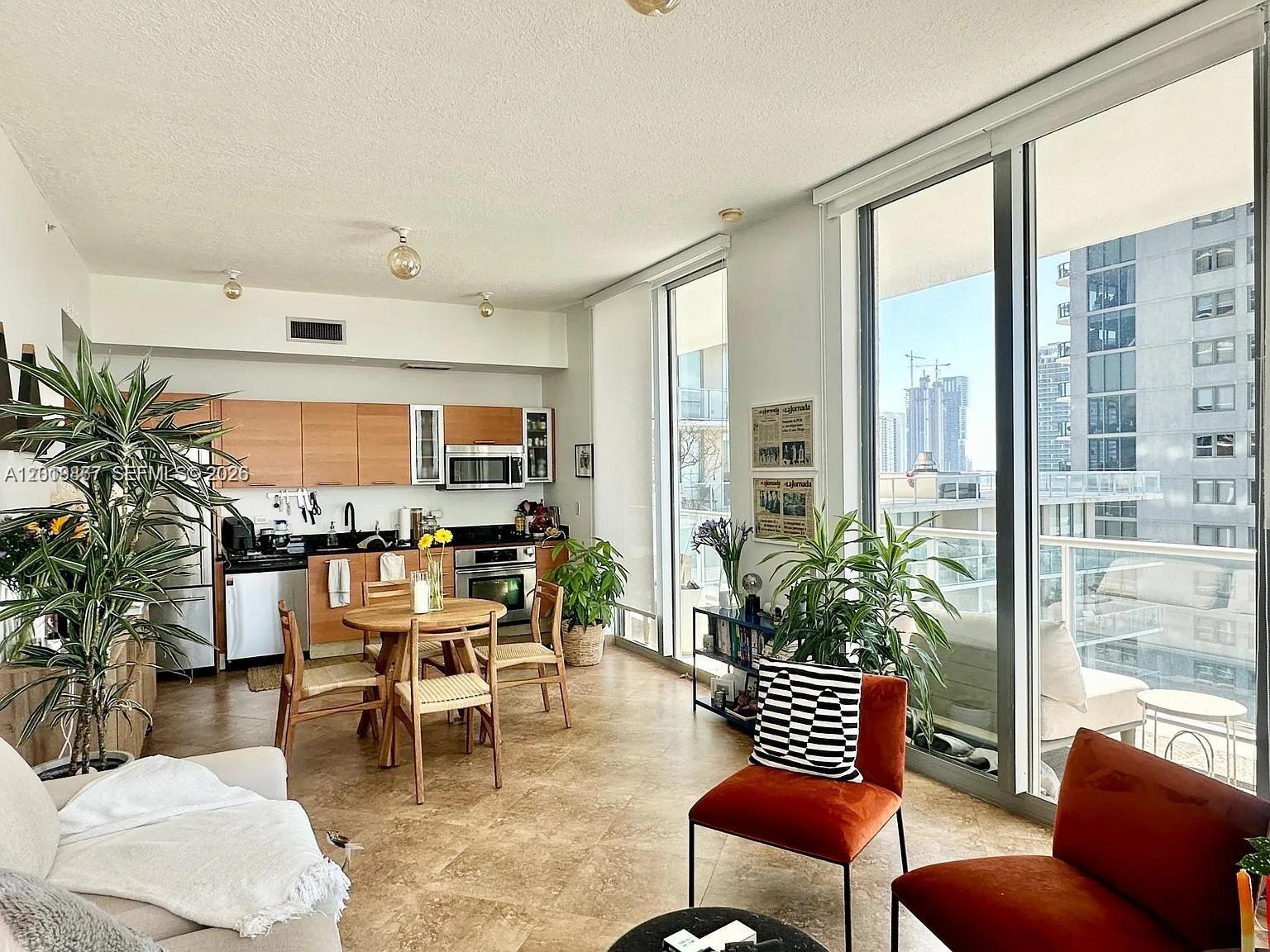 An open-concept living area features a kitchen with wood cabinets, tile floors, and floor-to-ceiling windows — 3470 E Coast Ave # H1805, Miami FL 33137, MIAMI, FL