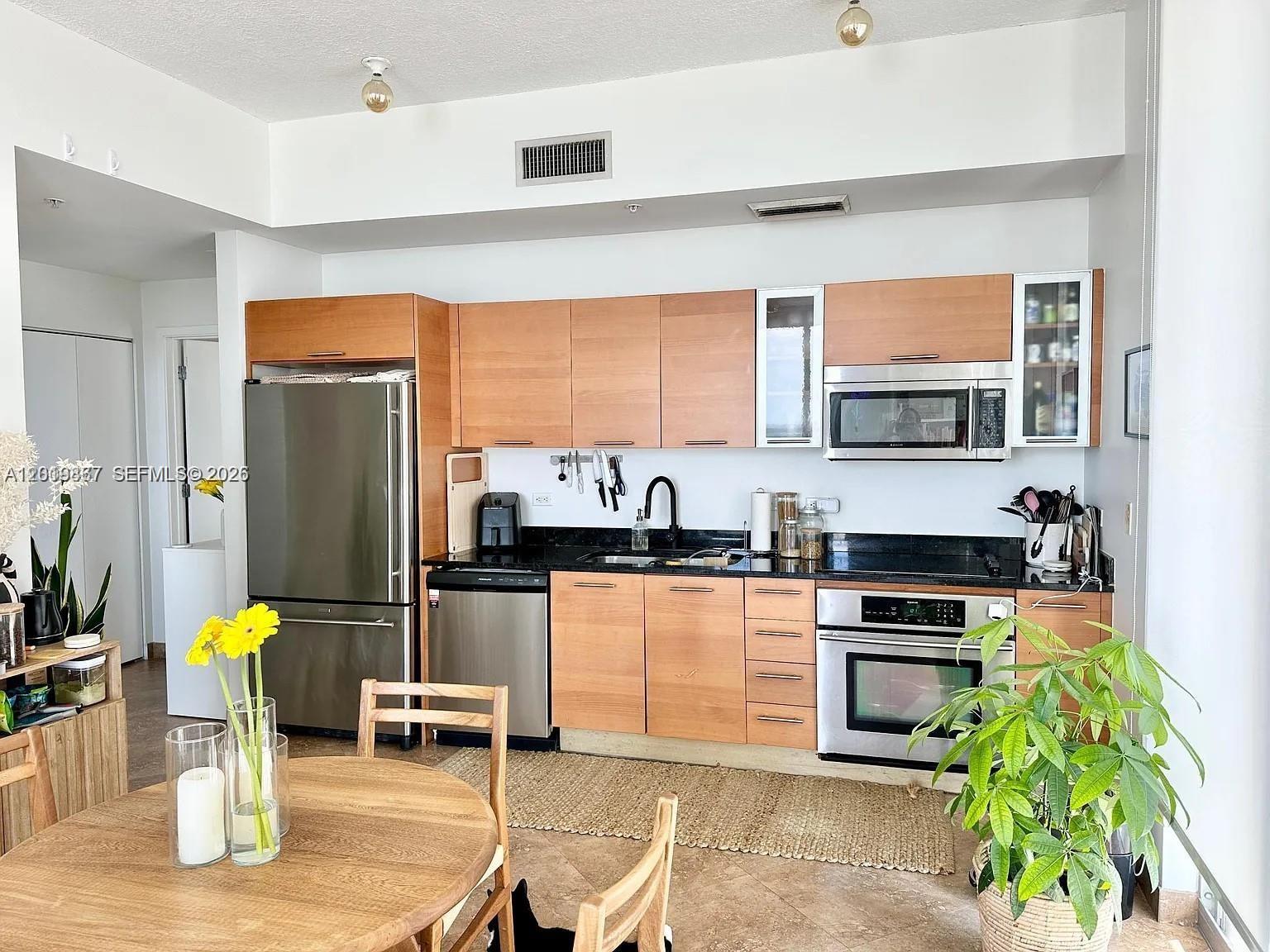 A kitchen features light wood cabinets, stainless steel appliances, and a black countertop — 3470 E Coast Ave # H1805, Miami FL 33137, MIAMI, FL