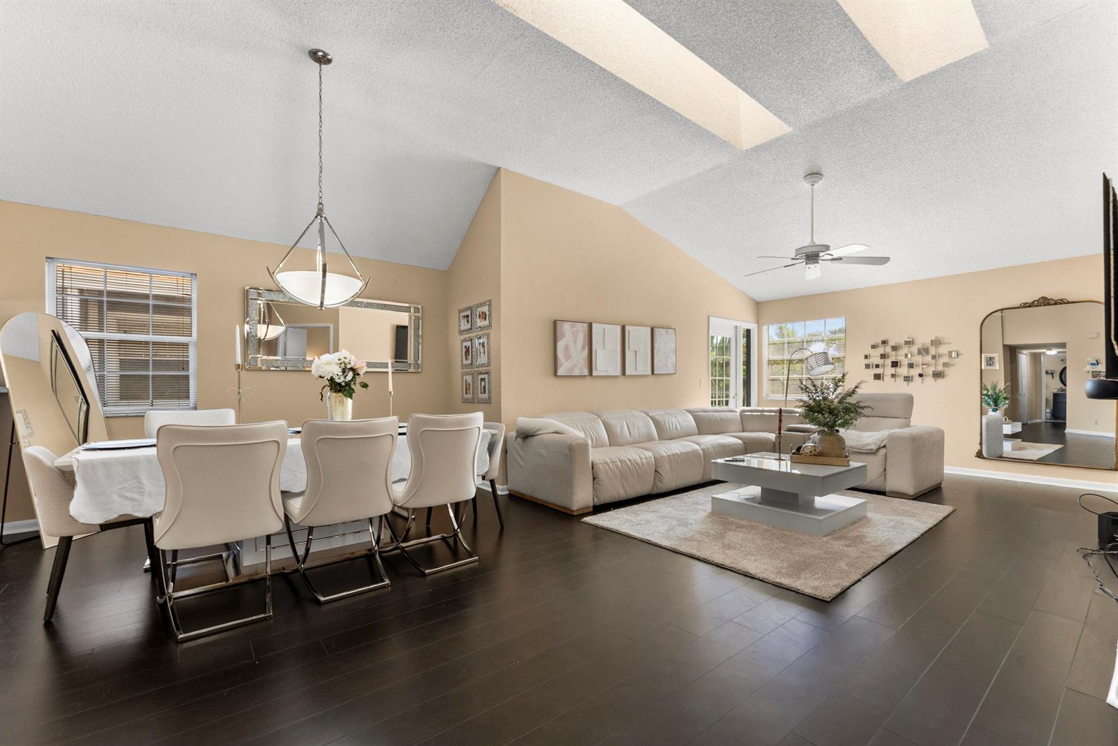 An open-concept living and dining area features vaulted ceilings, dark wood floors, and beige walls — 5359 Buckhead Circle # 2031, Boca Raton FL 33486, BOCA RATON, FL