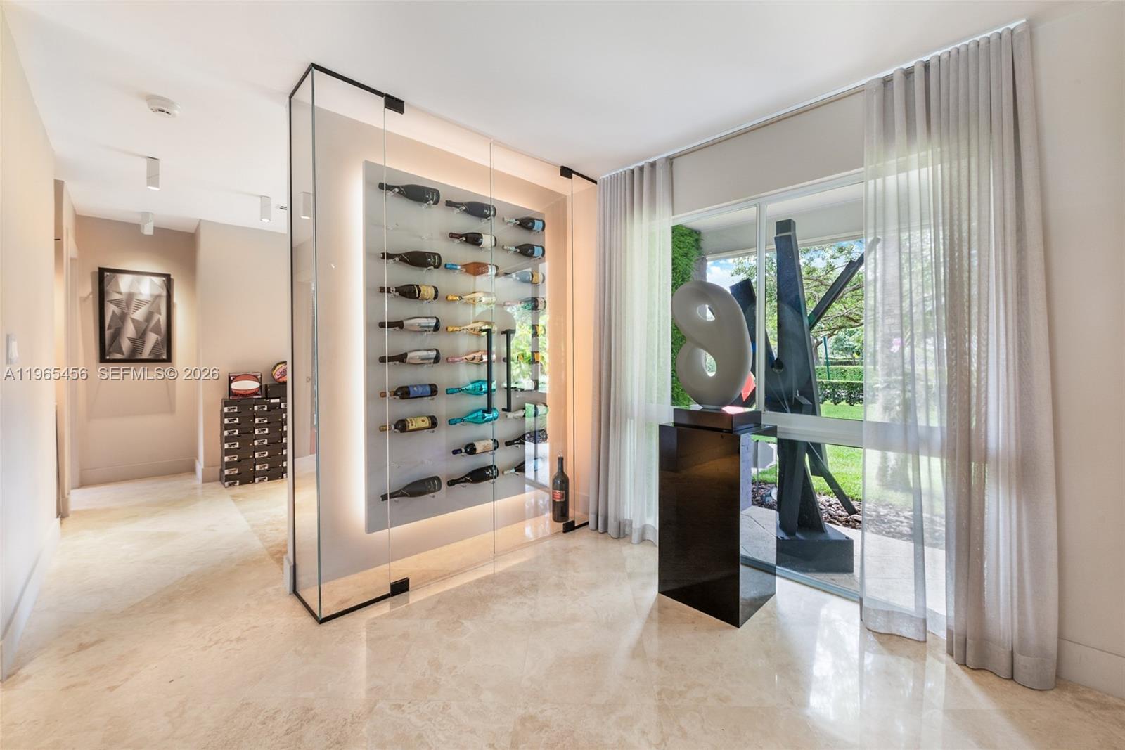 A modern room features a glass-enclosed wine display, marble flooring, and a large abstract sculpture — 7401 SW 117th St, Pinecrest FL 33156, PINECREST, FL