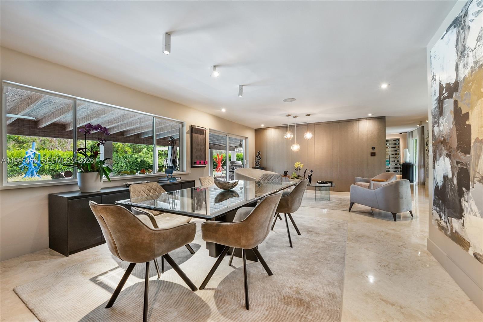 A modern dining room features a glass table, upholstered chairs, and large windows overlooking greenery — 7401 SW 117th St, Pinecrest FL 33156, PINECREST, FL