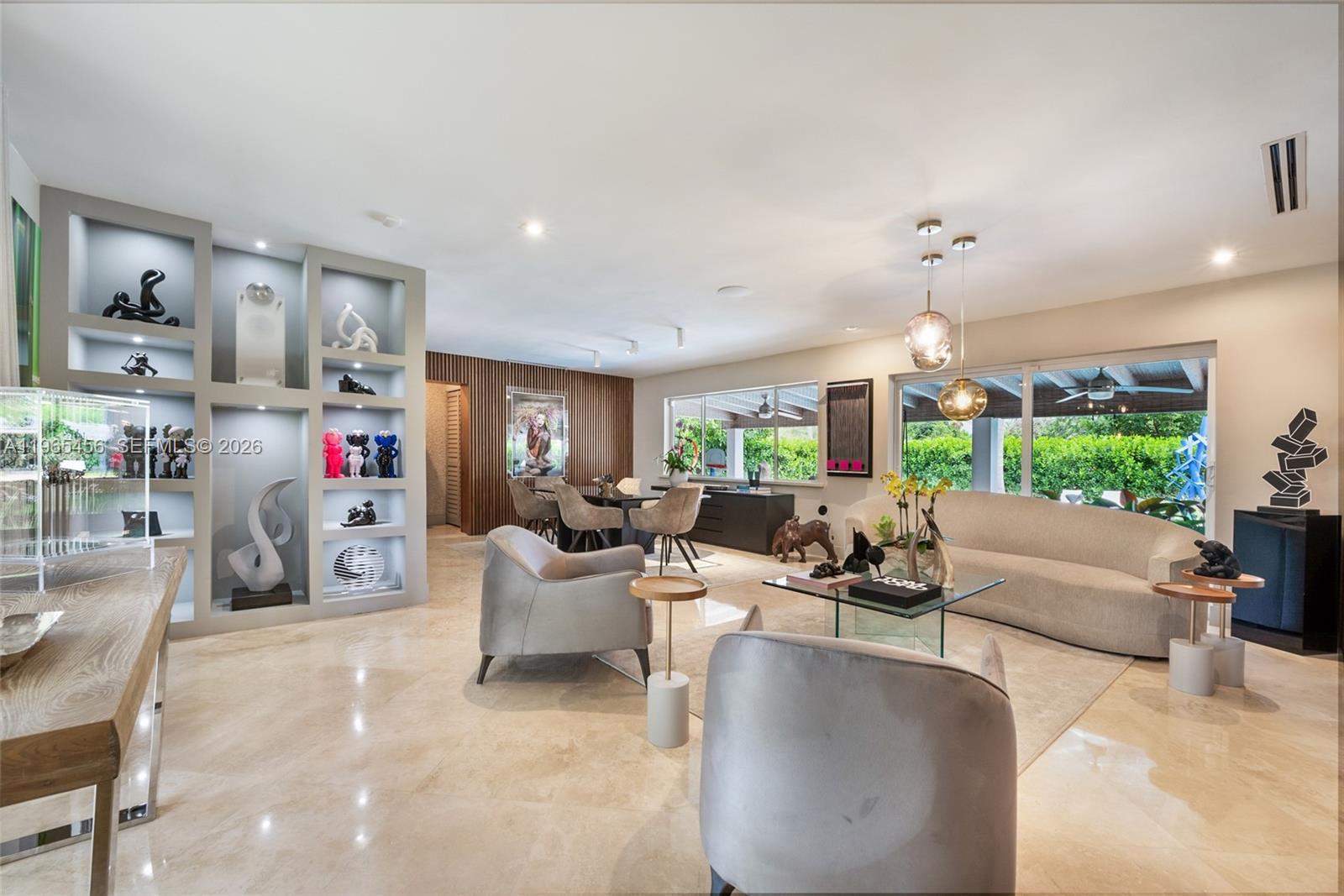 A modern living and dining area features marble floors, built-in shelving, and large glass doors — 7401 SW 117th St, Pinecrest FL 33156, PINECREST, FL