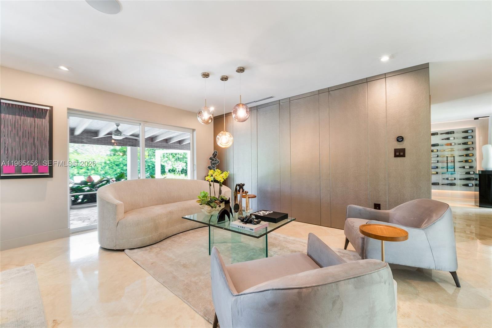 A modern living room features a curved sofa, glass coffee table, and a wine display wall — 7401 SW 117th St, Pinecrest FL 33156, PINECREST, FL