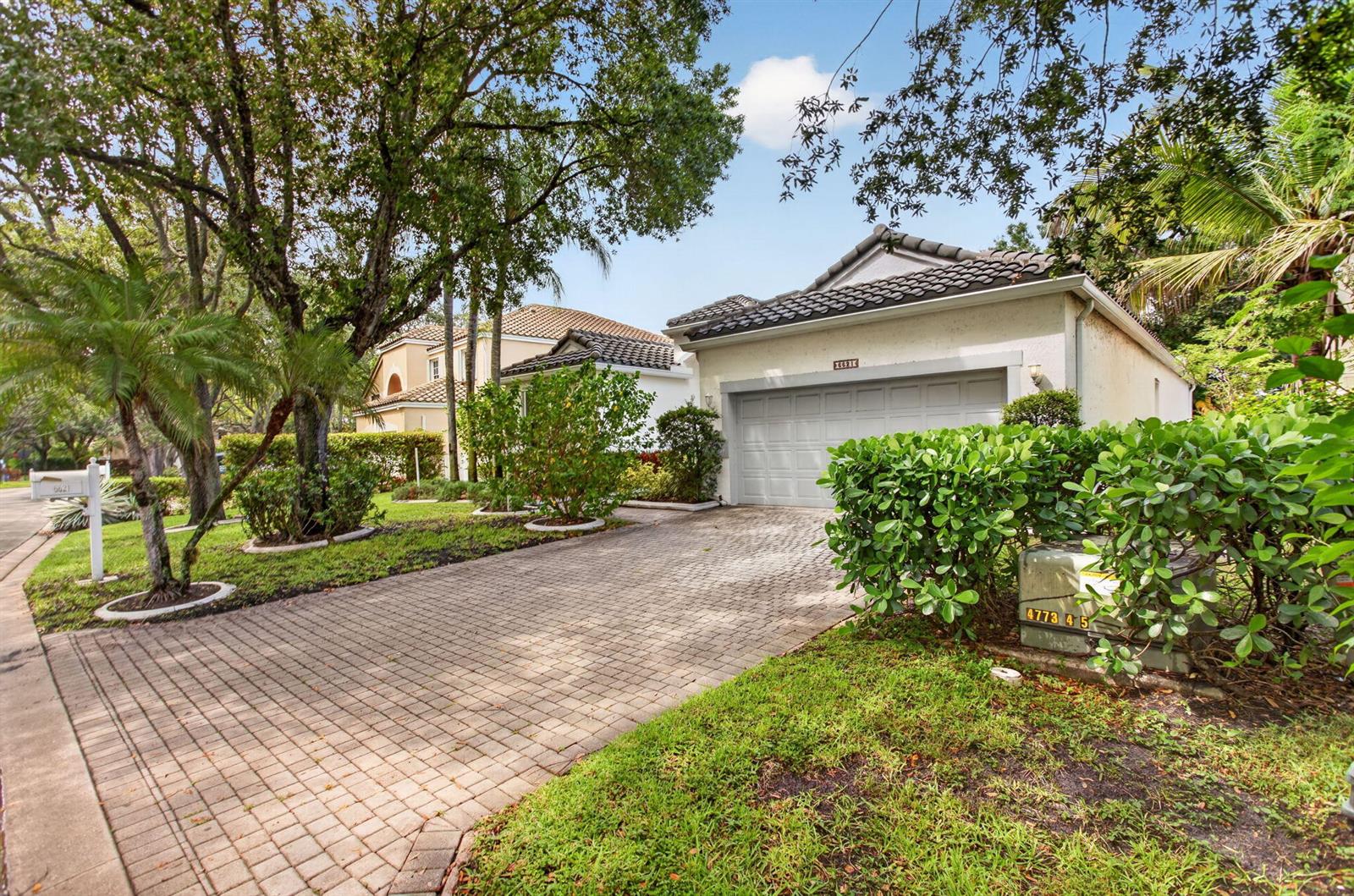 A paved driveway leads to a one-story house with a garage and lush landscaping — 6621 NW 78th Drive, Parkland FL 33067, PARKLAND, FL