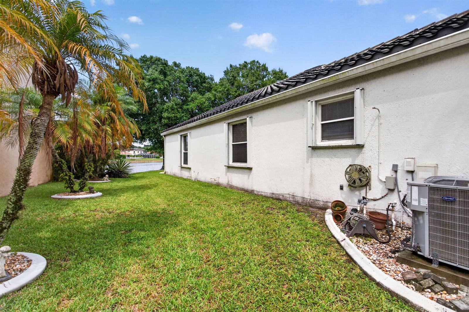 A side view of a white stucco house with a lawn, palm trees, and AC unit — 6621 NW 78th Drive, Parkland FL 33067, PARKLAND, FL
