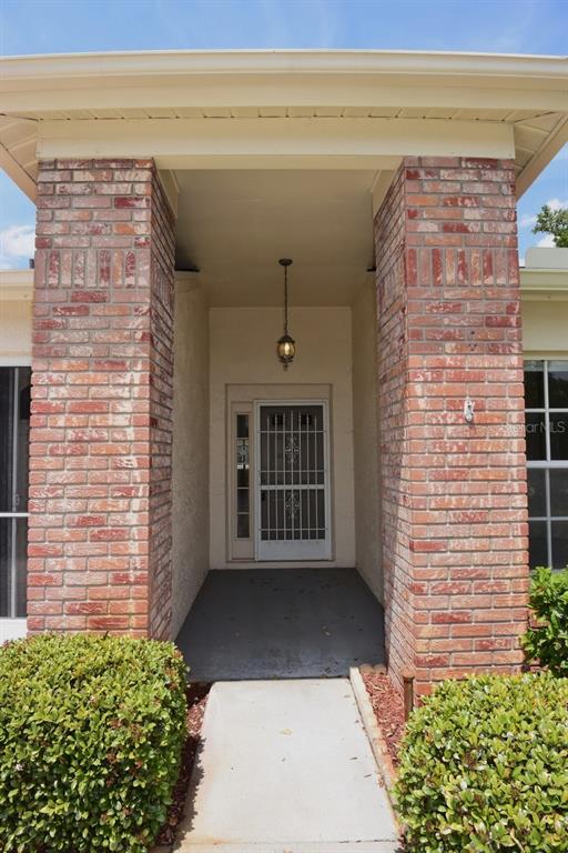 A concrete walkway leads to a covered front entryway flanked by two brick columns — 9027 WARWICK LANE, NEW PORT RICHEY, FL