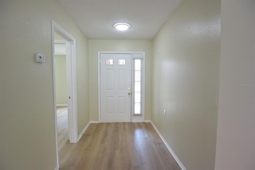 An entryway features light-colored walls, wood-look flooring, a white front door, and a ceiling light — 9027 WARWICK LANE, NEW PORT RICHEY, FL