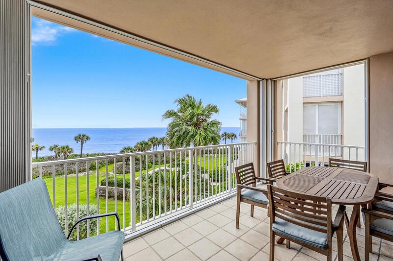 A balcony with a dining set overlooks a grassy lawn, palm trees, and the ocean — VERO BEACH, FL