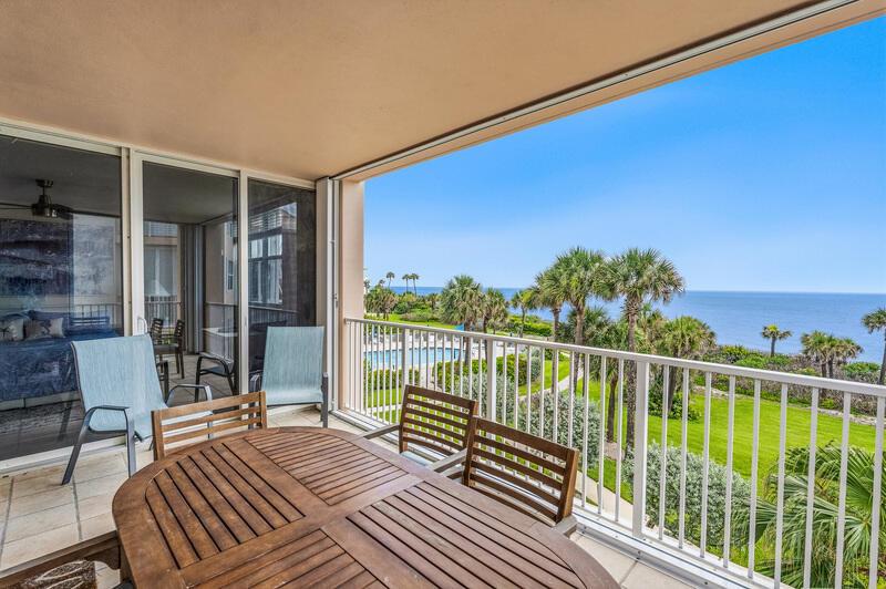 A balcony with a wooden table and chairs overlooks a lawn, palm trees, and ocean — VERO BEACH, FL