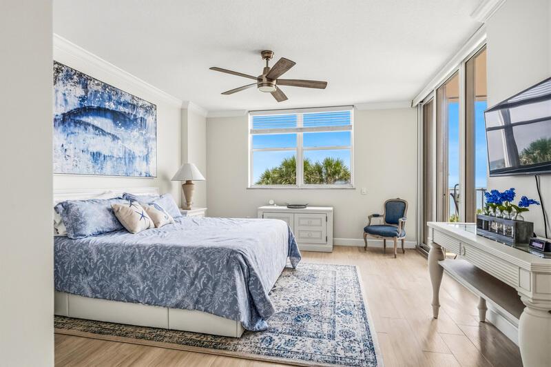 A bedroom features a king bed, blue patterned bedding, a ceiling fan, and ocean views — VERO BEACH, FL