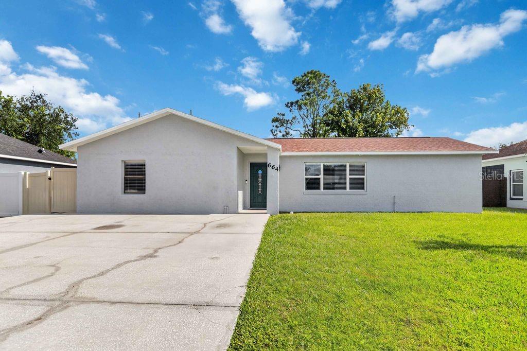 A single-story house with a gray stucco exterior, a concrete driveway, and a green front door — 664 MADRID DRIVE, KISSIMMEE, FL