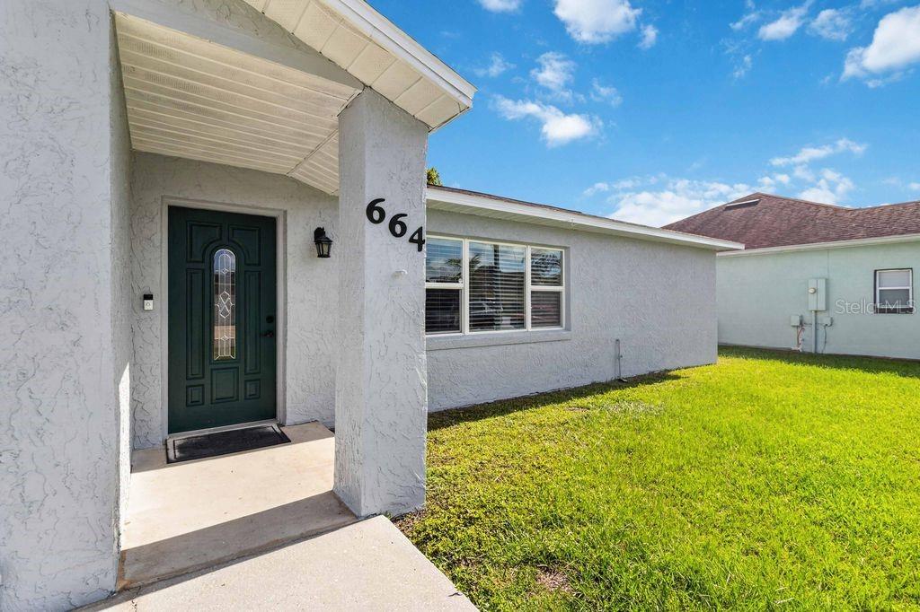 A light-colored house exterior features a covered entryway, a dark front door, and a lawn — 664 MADRID DRIVE, KISSIMMEE, FL