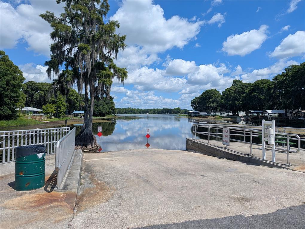 A concrete boat ramp leads into a calm lake surrounded by trees under a cloudy sky — 7633 S CRESCENT LOOP, FLORAL CITY, FL