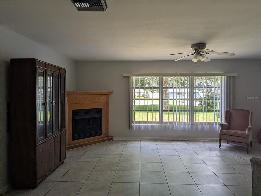 A living room features a corner fireplace, a large window with blinds, and tile flooring — 7633 S CRESCENT LOOP, FLORAL CITY, FL