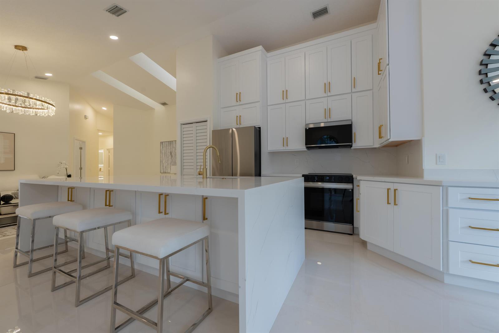 A modern white kitchen features a large waterfall island, gold hardware, and stainless steel appliances — 17277 Hampton Boulevard, Boca Raton FL 33496, BOCA RATON, FL