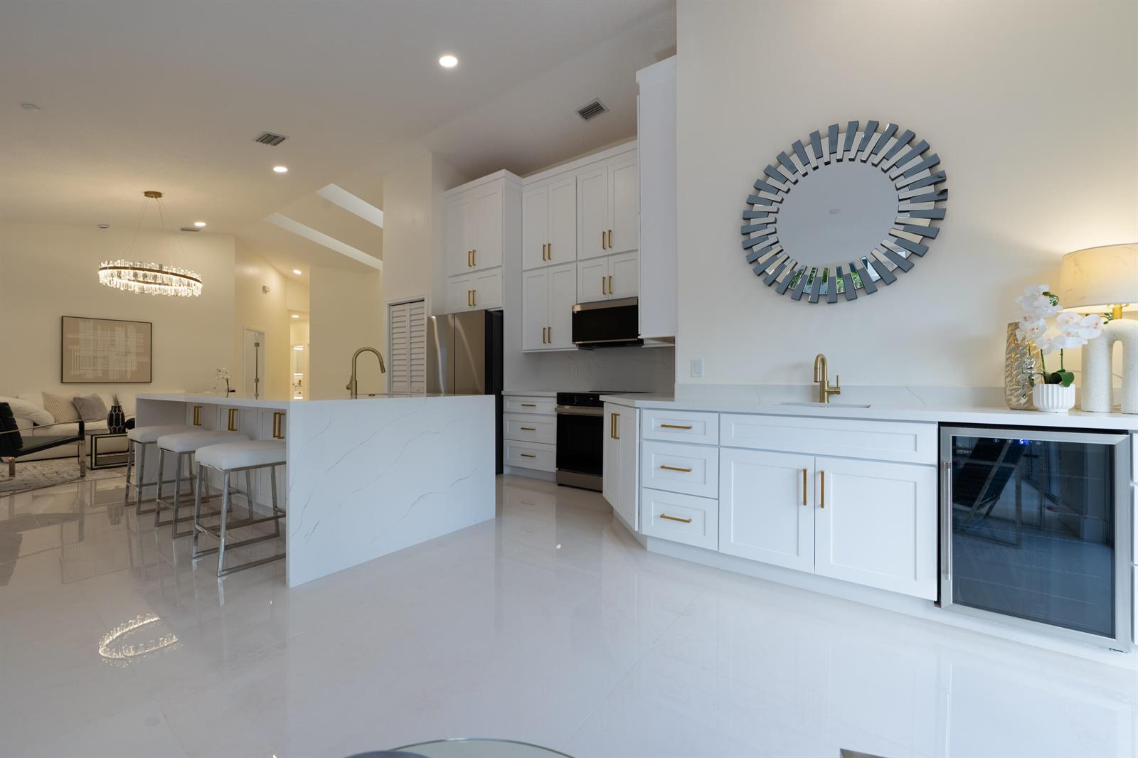 A modern white kitchen features a large waterfall island, gold hardware, and a wine cooler — 17277 Hampton Boulevard, Boca Raton FL 33496, BOCA RATON, FL
