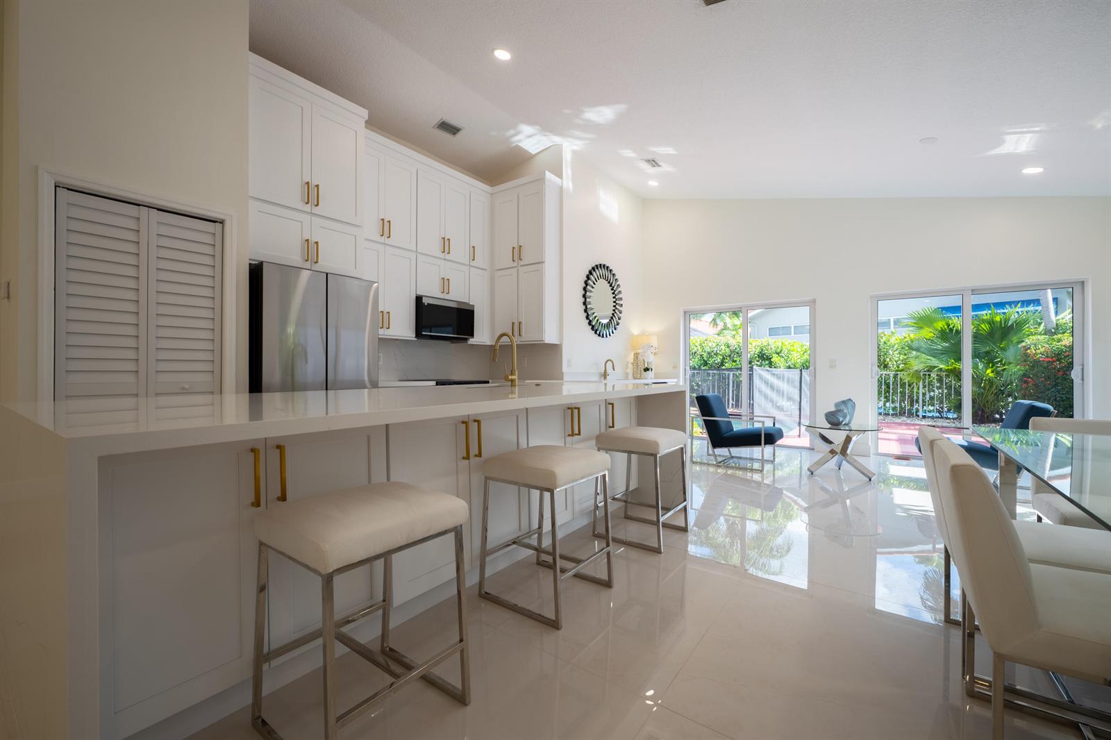A modern kitchen with white cabinets, gold hardware, and a breakfast bar overlooking a patio — 17277 Hampton Boulevard, Boca Raton FL 33496, BOCA RATON, FL