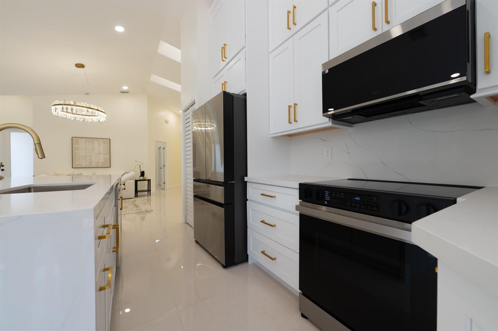 A modern kitchen features white cabinetry, gold hardware, stainless steel appliances, and a quartz island — 17277 Hampton Boulevard, Boca Raton FL 33496, BOCA RATON, FL