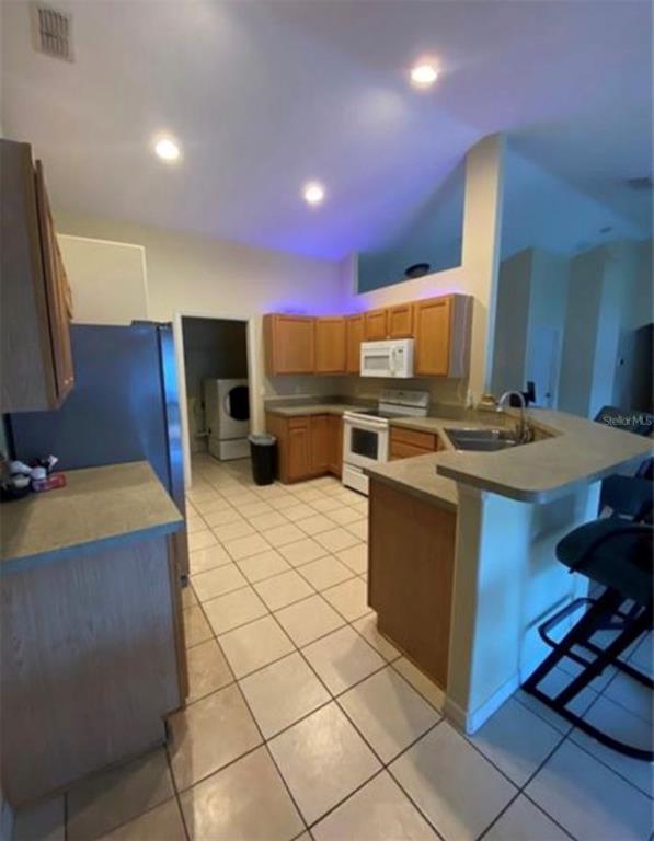 A kitchen with wooden cabinets, stainless steel appliances, and a breakfast bar overlooks a dining area — 8040 SW 128TH LOOP, OCALA, FL