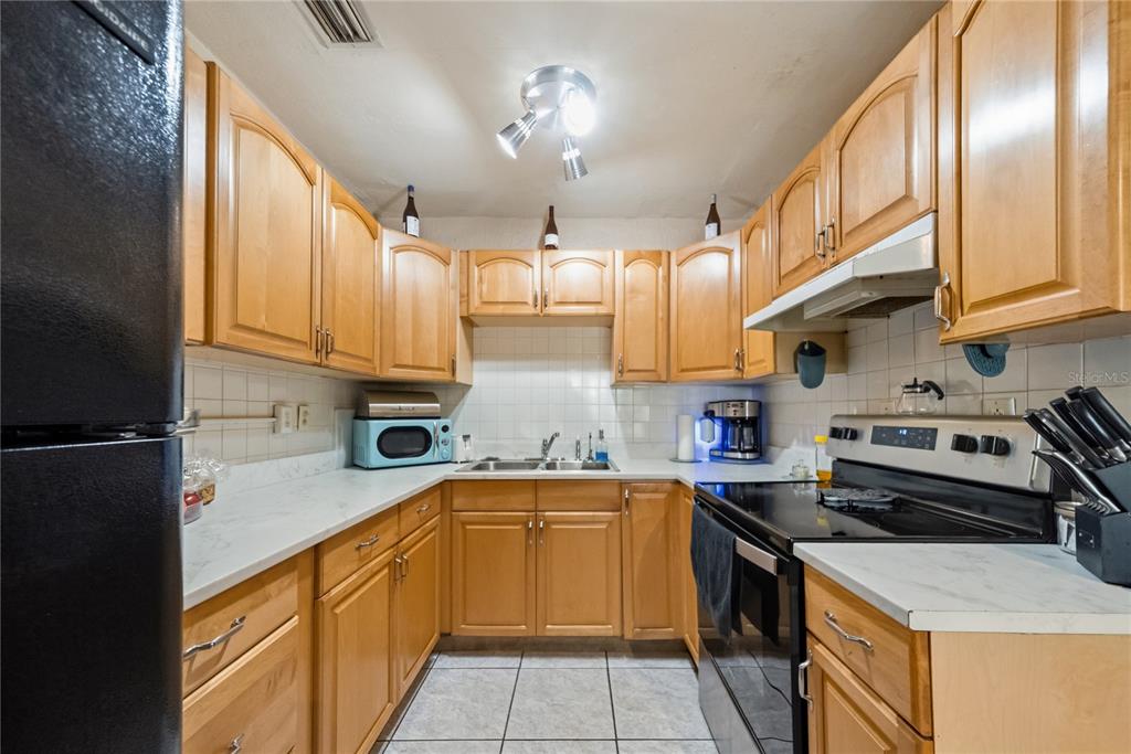 A kitchen features light wood cabinets, white countertops, a black refrigerator, and a black stove — 761 SEMINOLA BOULEVARD, CASSELBERRY, FL