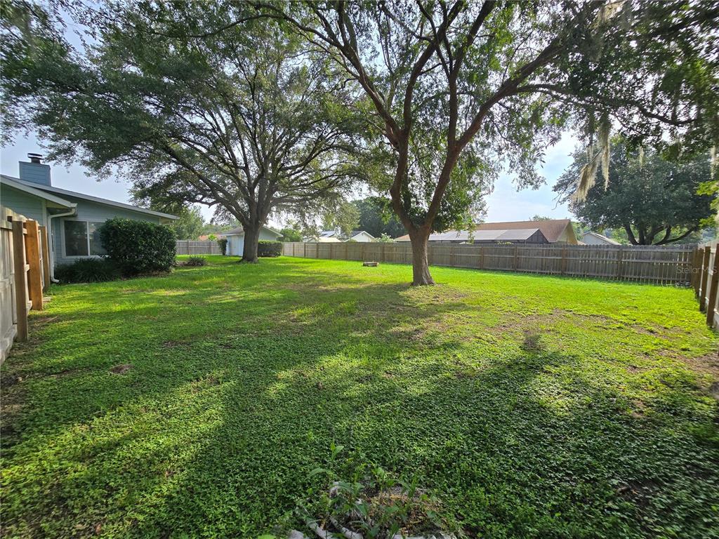 A spacious, grassy backyard features large mature trees and a wooden privacy fence — 5655 SE 42ND AVENUE, OCALA, FL