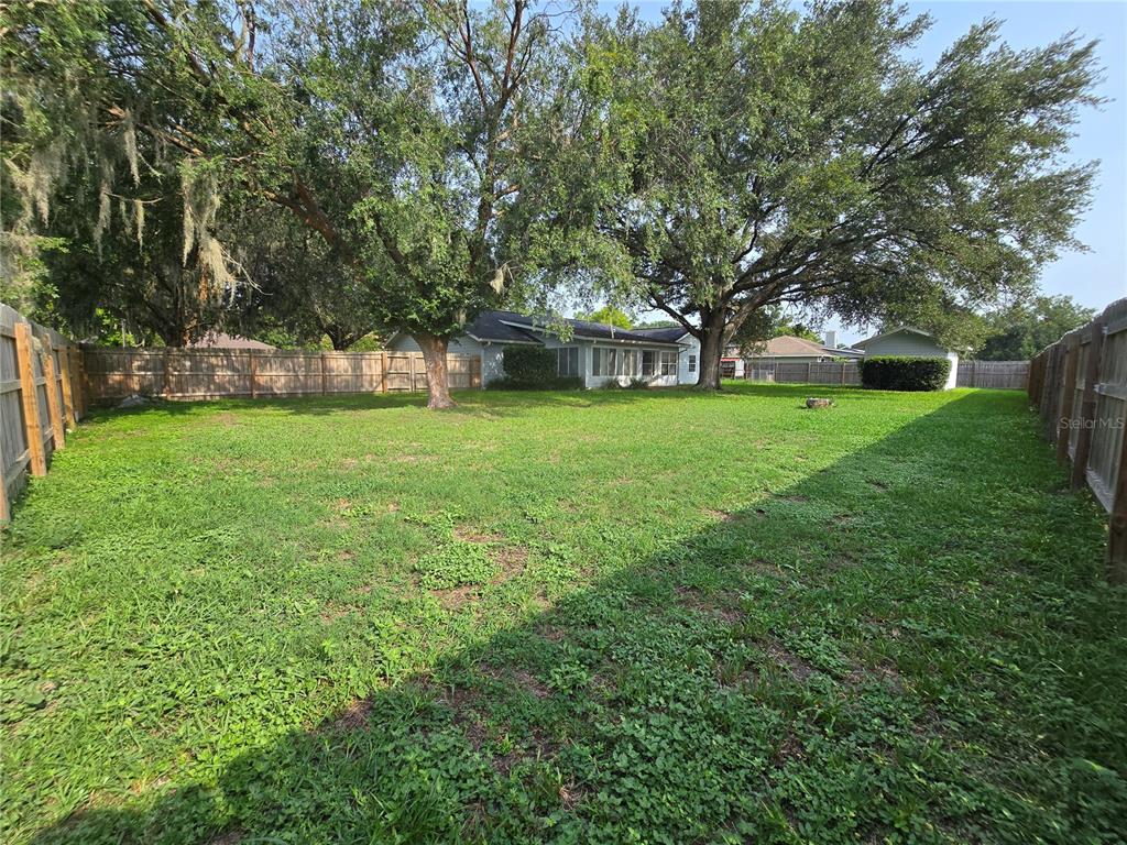 A large, grassy backyard features mature trees, a wooden fence, and a single-story house — 5655 SE 42ND AVENUE, OCALA, FL