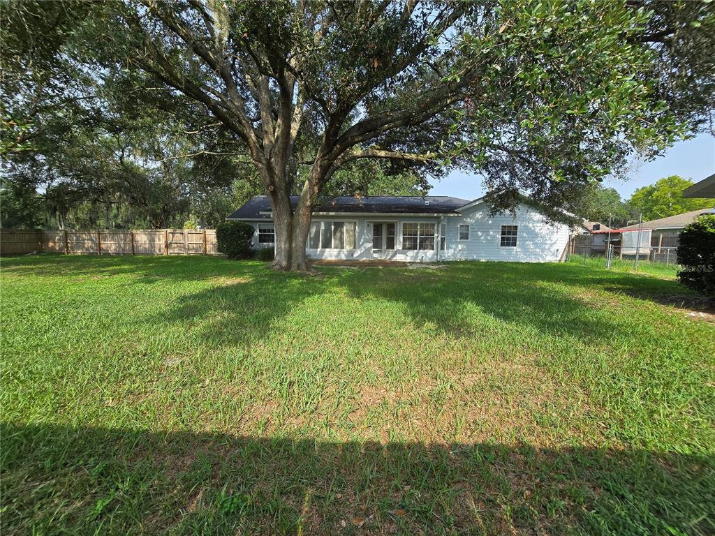 A backyard view of a single-story house with a large tree and wooden fence — 5655 SE 42ND AVENUE, OCALA, FL