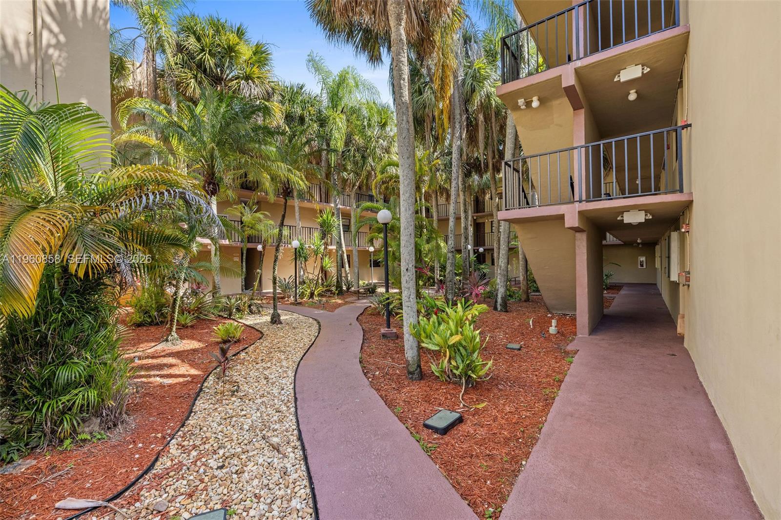 A paved walkway winds through a landscaped courtyard between multi-story apartment buildings with palm trees — 10835 SW 112th Ave # 305, Miami FL 33176, MIAMI, FL
