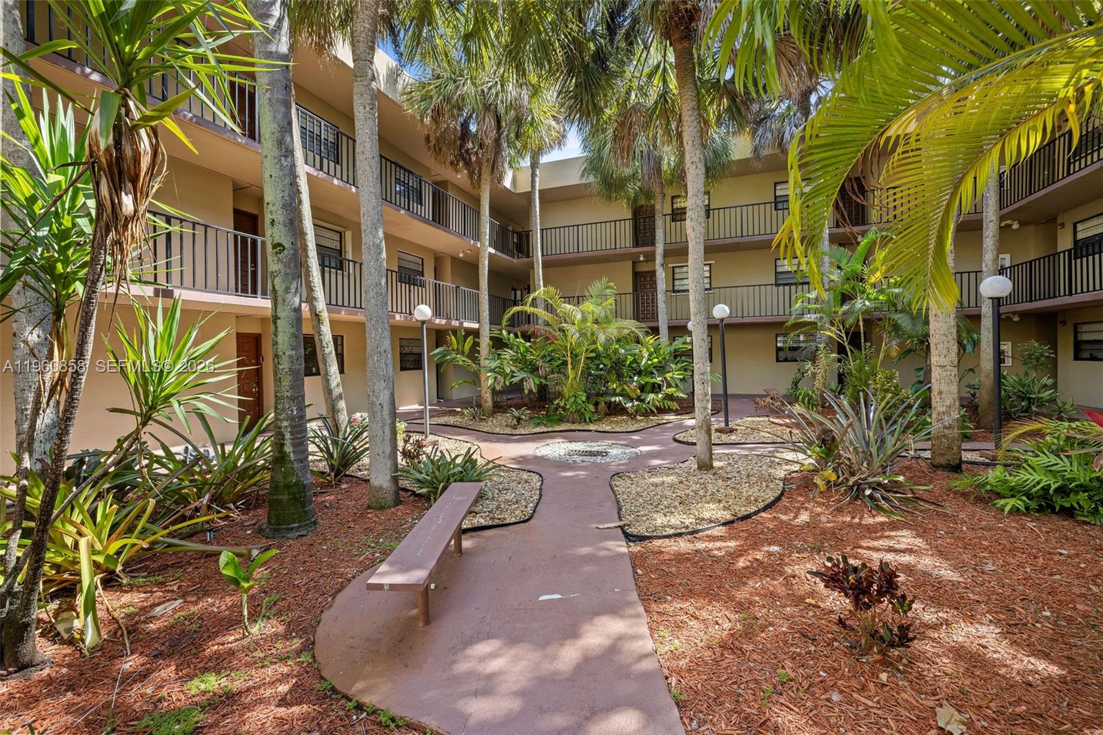 A courtyard with a paved path, a bench, and palm trees surrounded by apartment balconies — 10835 SW 112th Ave # 305, Miami FL 33176, MIAMI, FL