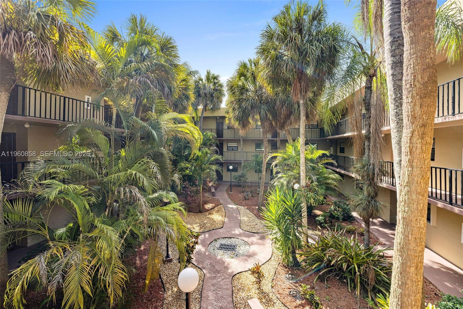 An outdoor courtyard features a paved walkway surrounded by palm trees and apartment building balconies — 10835 SW 112th Ave # 305, Miami FL 33176, MIAMI, FL