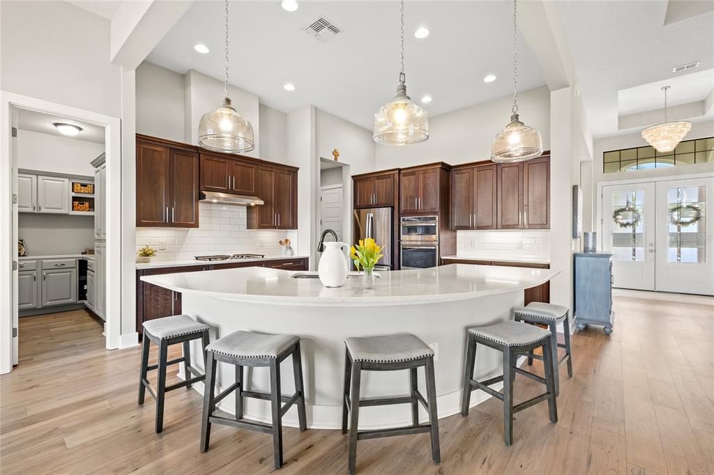 A kitchen with dark wood cabinets, a curved white island, and four gray bar stools — 25620 GRANDVIEW POINTE, SORRENTO, FL