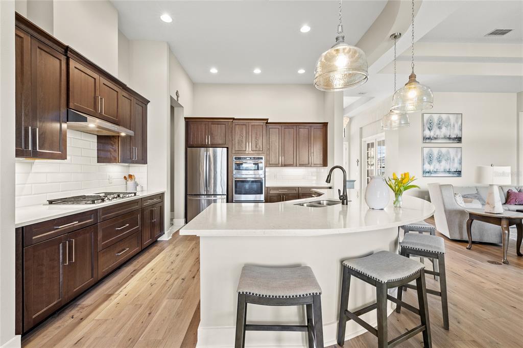 A modern kitchen features dark wood cabinets, white countertops, stainless steel appliances, and bar seating — 25620 GRANDVIEW POINTE, SORRENTO, FL