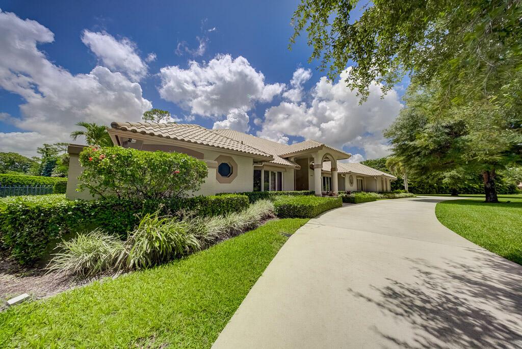 A single-story house with a tile roof and a long concrete driveway under a blue sky — 13406 Doubletree Circle, Wellington FL 33414, WELLINGTON, FL