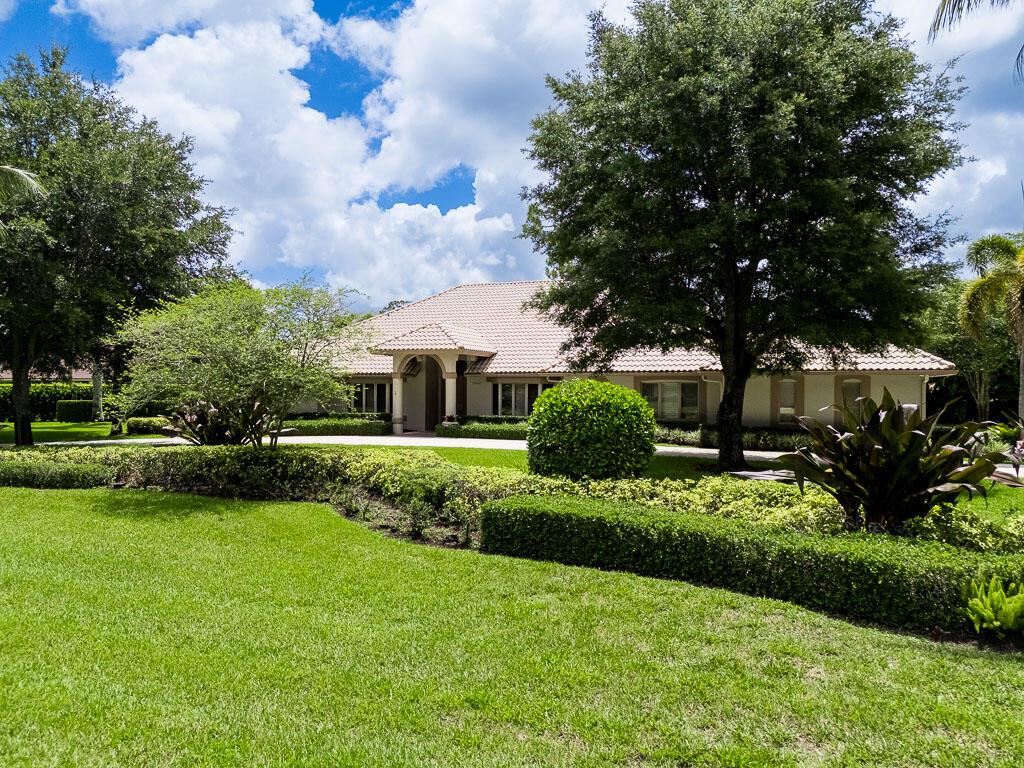 A single-story house with a tiled roof sits behind a manicured lawn and large trees — 13406 Doubletree Circle, Wellington FL 33414, WELLINGTON, FL
