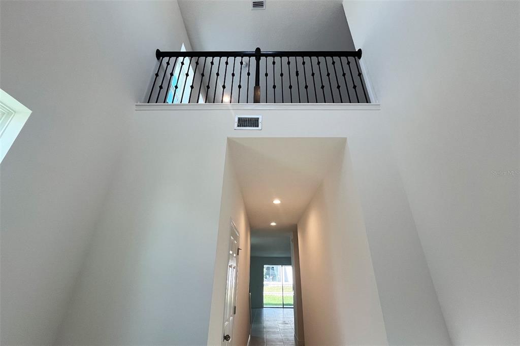 A high-ceilinged entryway features a dark metal railing overlooking a hallway with recessed lighting — 7036 ROLLING LEAF ROAD, GROVELAND, FL