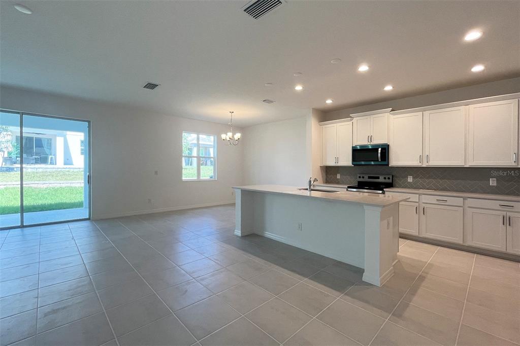 A kitchen with white cabinets, a central island, and tile flooring opens to a dining area — 7036 ROLLING LEAF ROAD, GROVELAND, FL