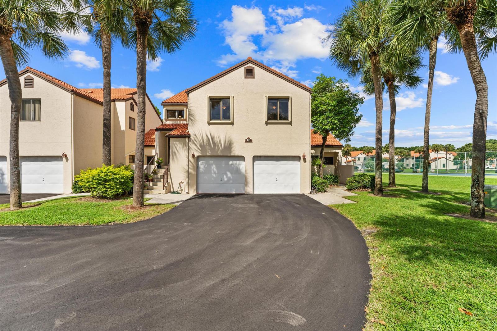 A two-story stucco townhouse features a two-car garage, tile roof, and palm trees in front — 18 Vía De Casas Sur # 205, Boynton Beach FL 33426, BOYNTON BEACH, FL