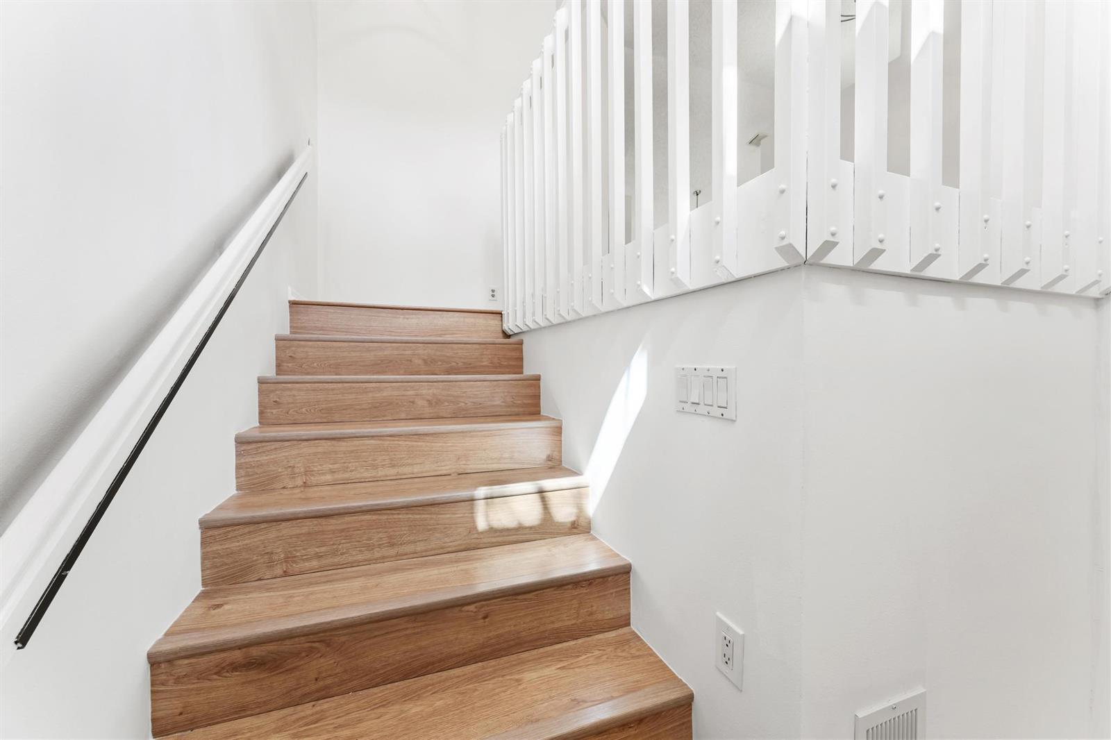 A wooden staircase with white railings and walls leads upward in a bright interior space — 18 Vía De Casas Sur # 205, Boynton Beach FL 33426, BOYNTON BEACH, FL