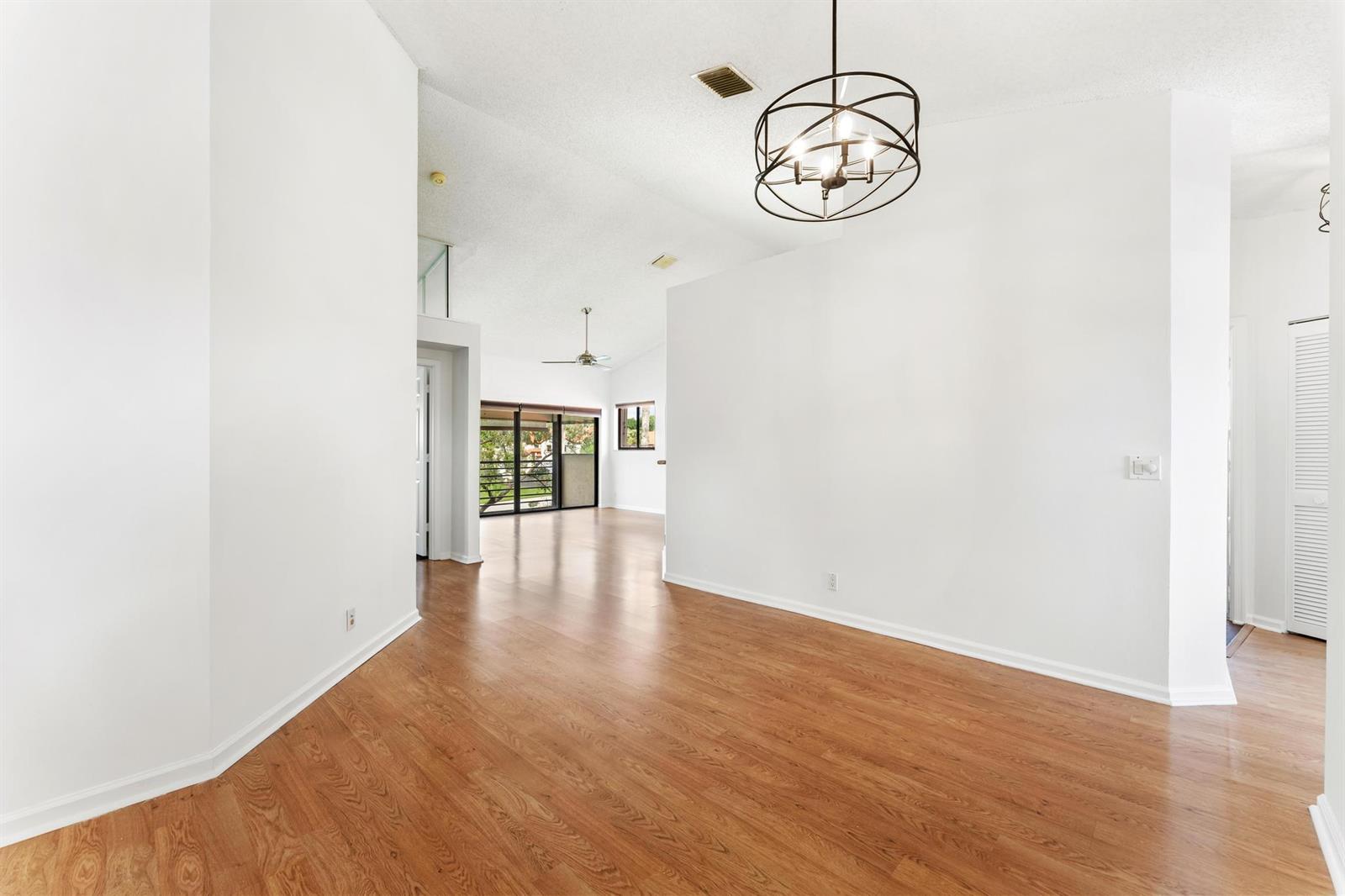 An empty room with wood-look flooring, white walls, and a modern circular chandelier — 18 Vía De Casas Sur # 205, Boynton Beach FL 33426, BOYNTON BEACH, FL