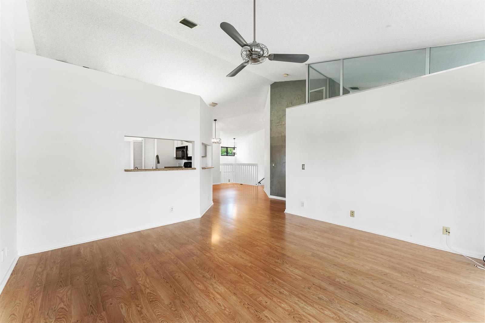 A spacious living room with hardwood floors, a ceiling fan, and a kitchen pass-through window — 18 Vía De Casas Sur # 205, Boynton Beach FL 33426, BOYNTON BEACH, FL