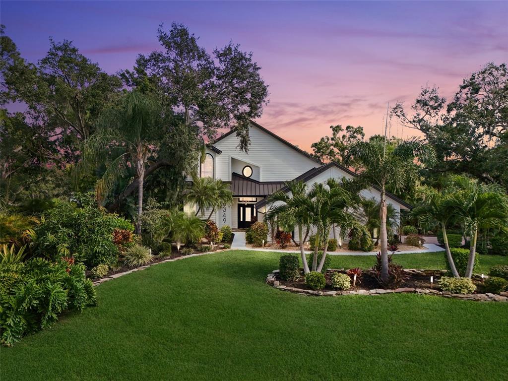 A two-story house with white siding and a dark roof sits behind a landscaped lawn — 6349 RAVENWOOD WAY, SARASOTA, FL