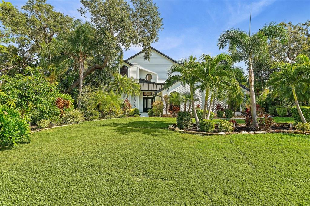 A white two-story house with a black roof and palm trees sits on a lawn — 6349 RAVENWOOD WAY, SARASOTA, FL