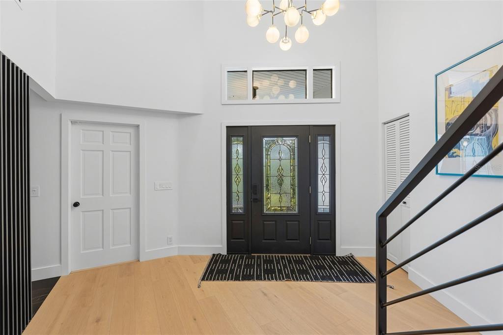 A bright entryway features light wood floors, a dark front door, and a modern chandelier — 6349 RAVENWOOD WAY, SARASOTA, FL