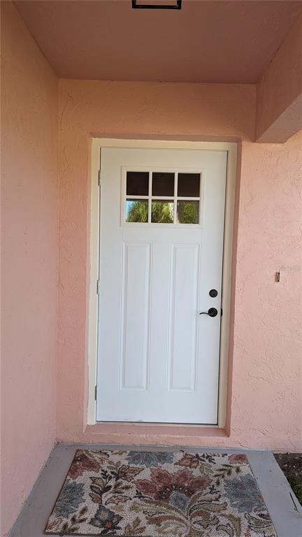 A white front door with a six-pane window sits within a peach-colored exterior entryway — 617 INDIANA AVENUE, NOKOMIS, FL